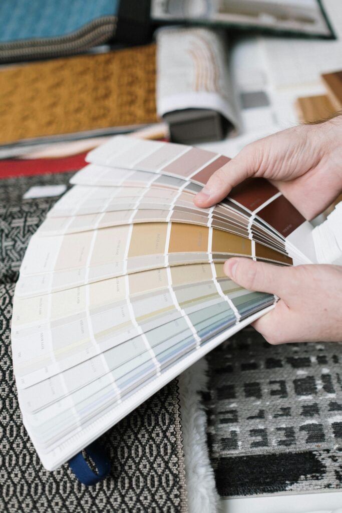 Hands holding a fan of color swatches against a backdrop of fabric samples, ideal for interior design projects.